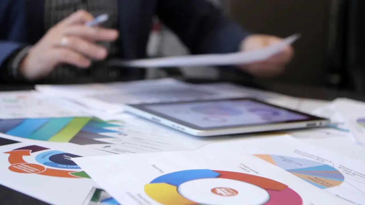 An instructor reviews printed charts beside a tablet at a desk.