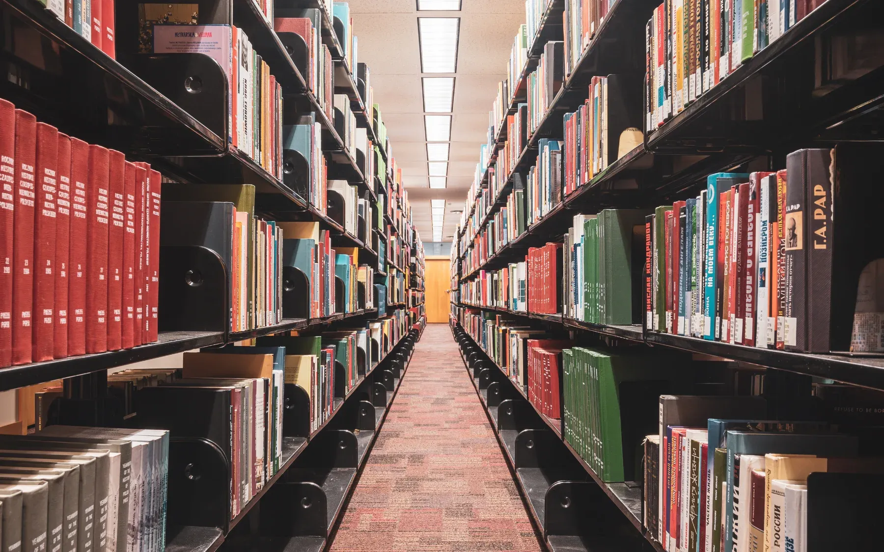 An aisle between library shelves packed with books.