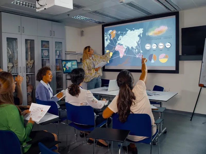 An instructor presents charts and a world map to a full classroom.